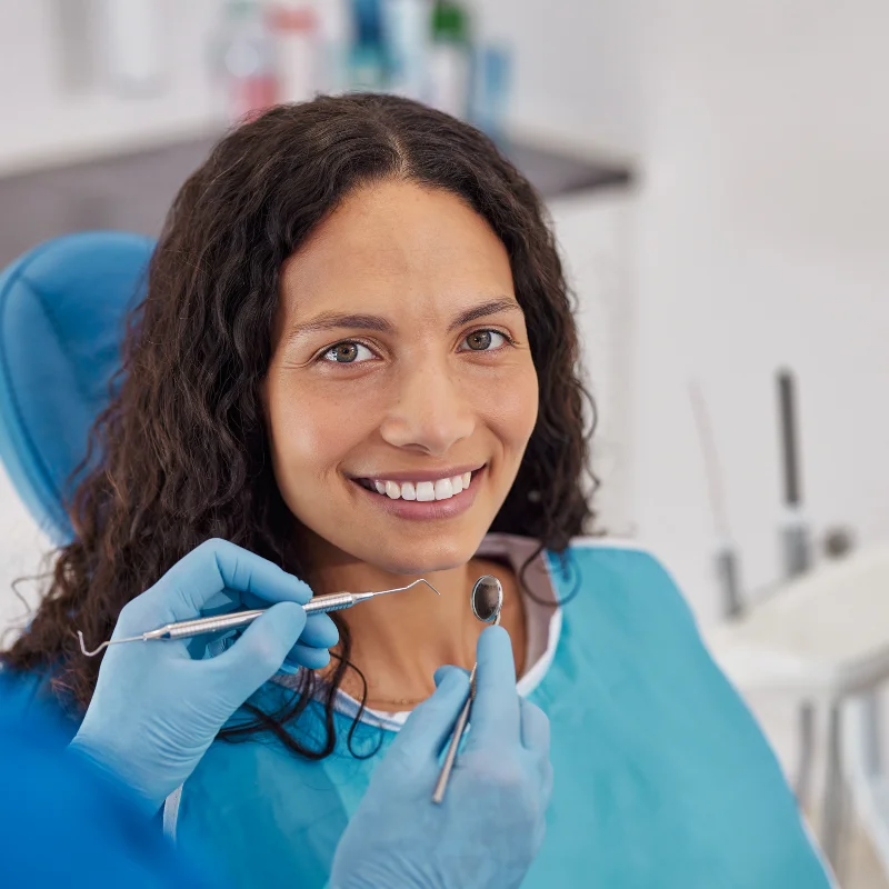 Smiling patient during a restorative dental examination while a dentist checks teeth with a mirror and scaler at Riverfront Dental in Cambridge Ontario