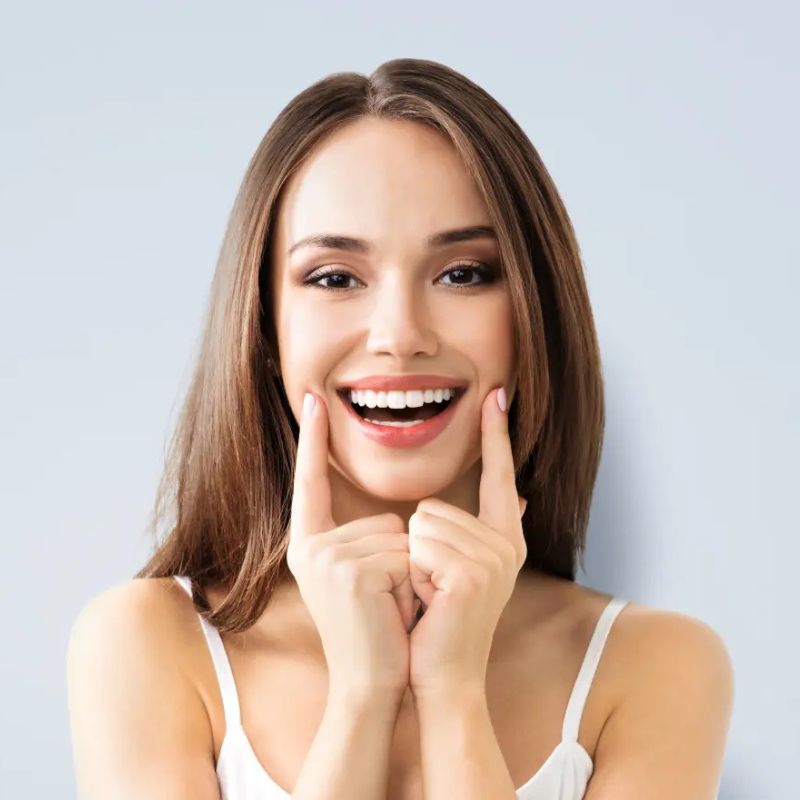 Young woman pointing to her teeth while smiling, representing patients seeking endodontic or root canal treatment at Riverfront Dental in Cambridge Ontario